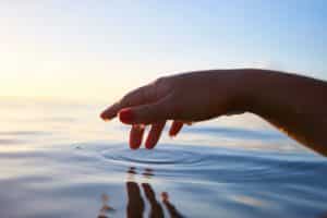 5 mindfulness techniques to calm down your day: A hand touches the surface of a calm pond.