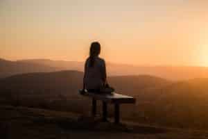 meditating for health: A woman sits on a cliff overlooking the sunset