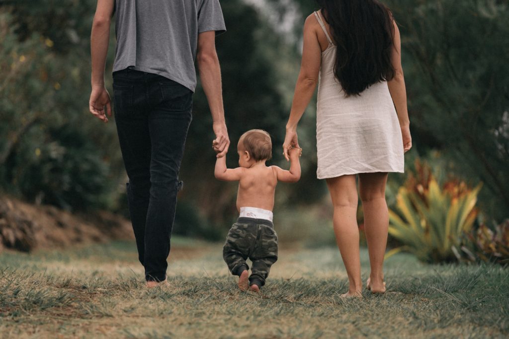 A lesson on being supported by others: A toddler stands in between his mother and a father holding their hands.