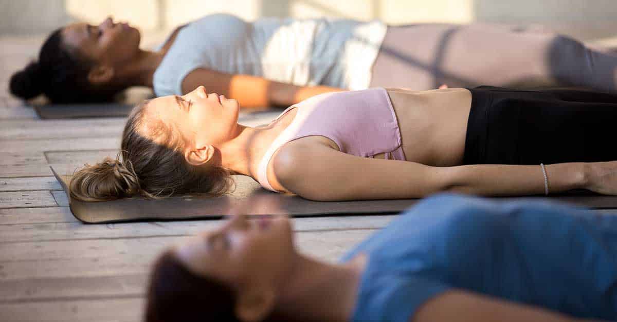 Group of young people practicing yoga lesson doing Dead Body, Savasana exercise, Corpse pose, working out, indoor close up, mixed race female students training at yoga studio. Well-being concept
